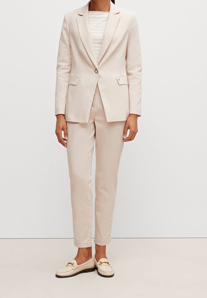 Jasnoróżowy garnitur z dopasowaną marynarką i prostymi spodniami, zestawiony z jasną koszulą w paski i kremowymi mokasynami z ozdobnym okuciem.