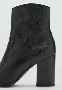 Schwarze Ankle Boots aus strukturiertem Leder, mit einer klaren Form, runder Zehenpartie und einem dicken Blockabsatz. Seitliche Aussparung vorhanden.