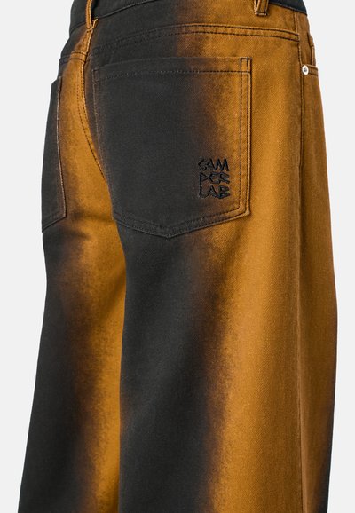 Jeans tinti di nero e arancione con effetto sfumato. Presentano una tasca posteriore con logo ricamato e dettagli di cucitura visibili.