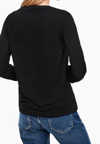 Svart långärmad topp med rundad halslinning. Tyget verkar slätt, med minimal detaljering och en avslappnad passform bak.