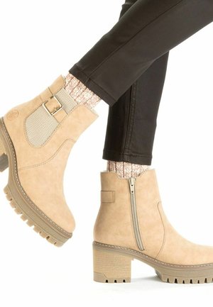 Beige ankle boots with a textured upper, side zipper, decorative buckle, and chunky heel. They feature a rubber sole and a smooth finish.