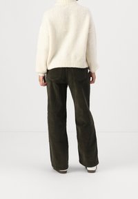 Pull en maille crème avec un col montant ; assorti à un pantalon large en velours côtelé vert olive foncé. Texture côtelée notable sur le pull.