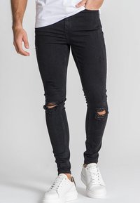 Vaqueros skinnies negros con desgarros en las rodillas, hechos de mezclilla, combinados con zapatillas de plataforma blancas. Camiseta blanca lisa.