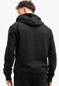 Zwarte hoodie met een ruime capuchon, geribde mouwen en zoom. Gemaakt van zachte stof, met een klein logo-label nabij de onderlinkerkant.