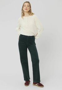 Pull en tricot texturé crème clair avec patte de boutonnage à trois boutons; pantalon en velours côtelé vert foncé; baskets en suède bourgogne avec accents blancs.