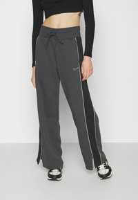Gray sweatpants with white side piping, drawstring waist, and slit hems, paired with black and white athletic shoes.