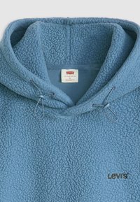 Haut à capuche en polaire bleu clair avec une texture ressemblant à un shag, doté d'une capuche avec cordon de serrage, d'un tissu texturé et d'un petit logo Levi's.