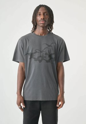 Gray cotton t-shirt featuring a subtle black abstract pattern and a round neckline. Short sleeves with a loose fit.