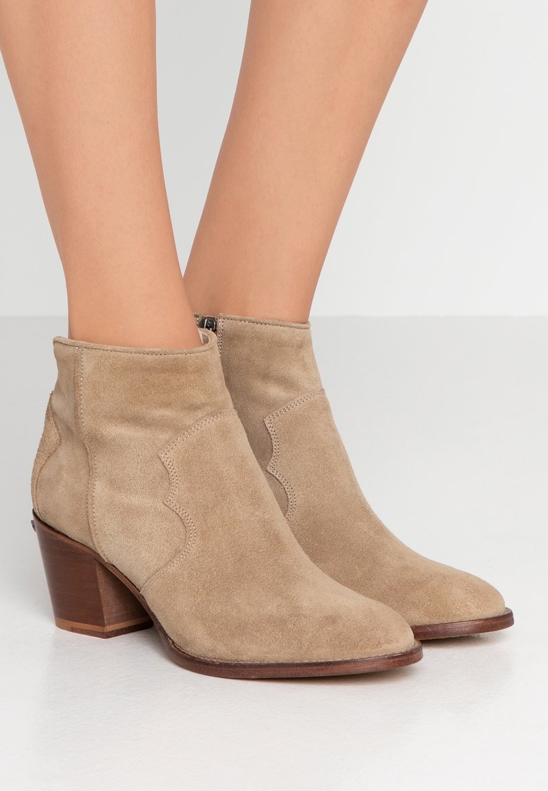 Beżowe zamszowe botki za kostkę z wydłużonym noskiem, zaokrąglonymi szwami bocznymi oraz niskim, drewnianym obcasem. Zamek błyskawiczny z tyłu. Gładka struktura.