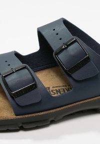 Navy blue sandal with two wide straps, black metal buckles, and a cork footbed, featuring a textured surface and rubber sole.