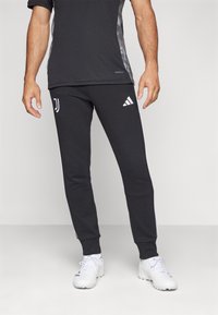 Černé sportovní kalhoty s bílým logem Adidas a emblémem Juventusu, které mají úzký střih, měkkou texturu a kontrastní boční pruhy.