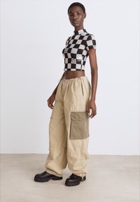 Crno-bijeli karirani crop top s kratkim rukavima, u kombinaciji s bež cargo hlačama koje imaju veliki maslinasto zeleni bočni džep. Crne chunky cipele.