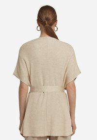 Beige stickad kortärmad cardigan med lös passform och ett matchande bälte i midjan. Texturerat tyg med en subtil glansdetalj.