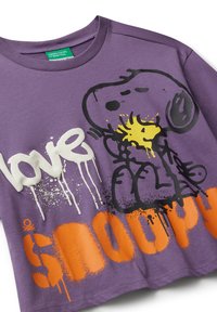Fialové tričko s potiskem Snoopyho objímajícího Woodstocka, slovo "Láska" v bílé barvě a "Snoopy" velkým oranžovým graffiti-style textem.