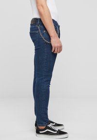 Slim-fit farkut sinistä farkkukangasta, joissa on ketjuviimeistely, napin ja vetoketjun sulku sekä nahkainen vyötärönauha. Yhdistetty mustiin lenkkareihin.