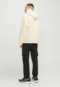 Cream fleece hooded sweatshirt with a textured finish, paired with black cargo pants featuring side pockets and elastic cuffs. Black athletic shoes.