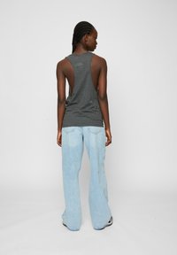 Grå ærmeløs top med åben ryg, parret med lyseblå flare jeans. Stoffet ser blødt ud med en afslappet pasform.