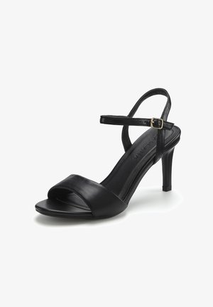 Schwarze High-Heel-Sandale aus Leder mit einem vorderen Riemen, einem Knöchelriemen und einer goldenen Schnalle vor weißem Hintergrund.