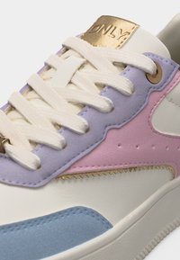 Κοντινό πλάνο αθλητικού παπουτσιού με λευκά κορδόνια, πάνελ σε παστέλ αποχρώσεις μωβ, ροζ και μπλε, και χρυσή ετικέτα με χαραγμένη τη λέξη "ONLY" στη γλώσσα.