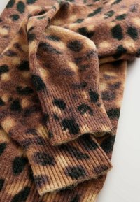 Tissu tricoté brun et beige duveteux avec des taches de léopard noires irrégulières et des poignets côtelés pliés sur une surface blanche.