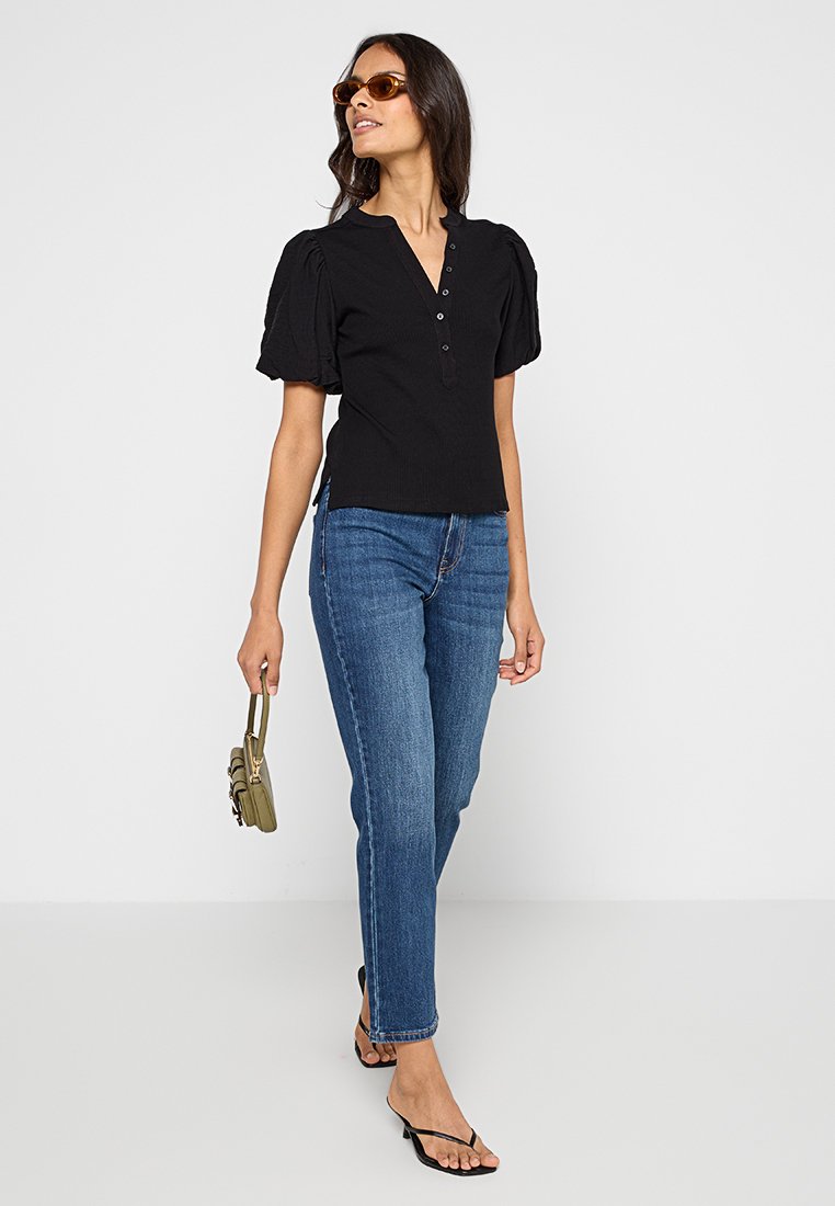 Top negro acanalado con mangas abullonadas y un escote en V pronunciado, con detalles de botones. Combinado con jeans rectos azules y sandalias negras de tiras.