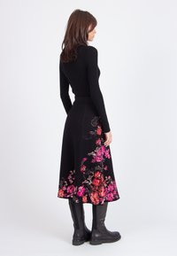 Maglietta nera a maniche lunghe abbinata a una gonna nera svasata fino al ginocchio, decorata con vivaci ricami floreali rosa e rossi all'orlo. Stivali neri al ginocchio.