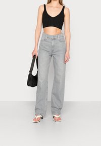 Černý žebrovaný crop top, světle šedé džíny s vysokým pasem, bílé sandály na podpatku a malá černá kabelka. Styl je ležérní a moderní.