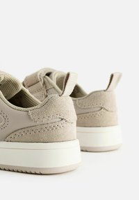 Beige Sneaker mit einer Kombination aus glattem Leder und Wildledertexturen. Verfügt über eine gepolsterte Ferse und eine weiße Gummisohle mit Rutschfestigkeitsmuster.