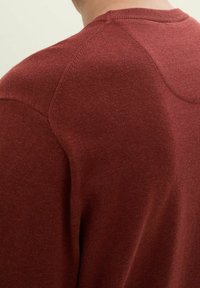 Bordó kötött pulóver kerek nyakkivágással, sima textúrával és raglánujjakkal, amelyeken enyhe varrási részlet található a vállon.
