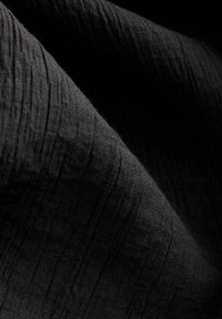 Čierna textúrovaná látka s jemnými lineárnymi vzormi, ktorá vykazuje jemný, tkaný vzhľad a hladký, matný povrch.