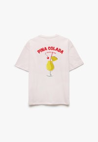 Lys pink bomulds t-shirt med et grafisk motiv af en piña colada med et kirsebær og et sugerør samt rød tekst "PINA COLADA A FRESH DRINK." Korte ærmer.
