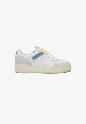 Zapatilla deportiva blanca de corte bajo con detalles en gamuza gris claro, suela beige, cordones crema y una etiqueta azul en el lateral que dice "Edición Oro".