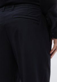 Čierne nohavice na mieru s hladkou textúrou látky, bočnými vreckami a diskrétnym logom "BOSS" vyrazeným na zadnom vrecku.