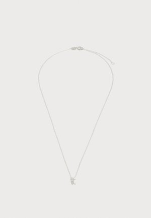 Collier délicat en chaîne argentée avec un petit pendentif lettre « t » et une fermeture à mousqueton sur fond blanc uni.