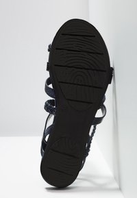 Sandale bleu marine avec une semelle en caoutchouc noir texturée. Lanières en matériaux tressés et lisses. Taille 37 indiquée sur la semelle.