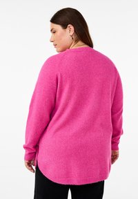Fuchsia knitted sweater with a rounded hem, side slits, and long sleeves, featuring a soft texture and relaxed fit.