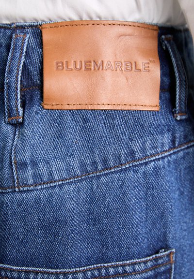 Blaue Denim-Jeans mit einem braunen Lederpatch, auf dem "BLUEMARBLE" steht. Mit sichtbaren Nähten und einem Taschen-Detail.