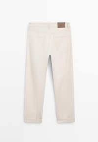 Rückenansicht von beigen, gerade geschnittenen Hosen mit umgeschlagenen Säumen, Gürtelschlaufen, zwei Gesäßtaschen und einem braunen Markenlabel am Bund.