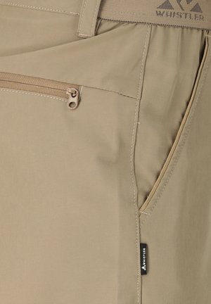 Beige broek bijna close-up met een zak met rits, zijzak met split, gedetailleerd stiksel en een klein zwart Whistler-merklabel.