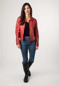 Rode leren jas met een kraag, strakke pasvorm en ritssluiting; gedragen over een zwarte top en aangevuld met blauwe spijkerbroek en zwarte kniehoog laarzen.