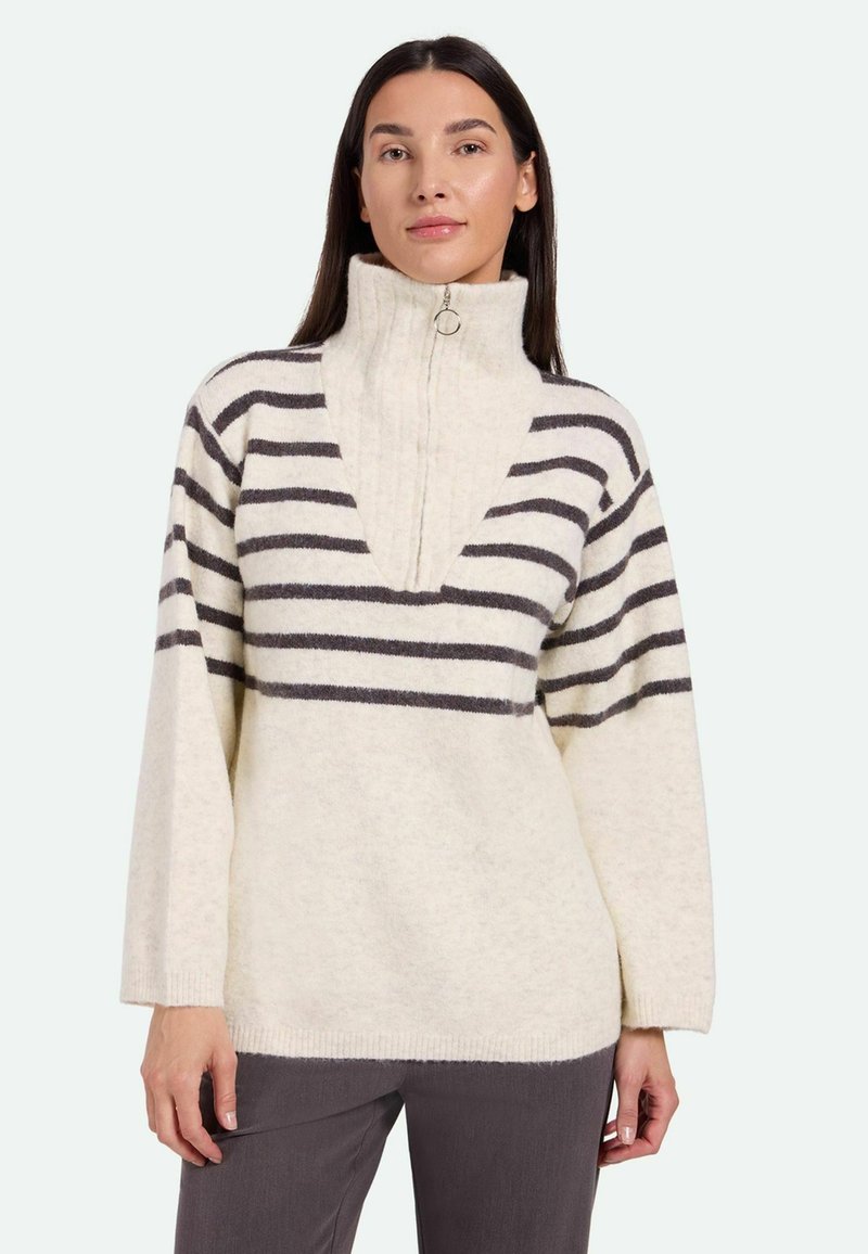 Pullover di colore crema con colletto alto e zip a metà, caratterizzato da strisce orizzontali grigio scuro e una scollatura a V. Texture morbida.