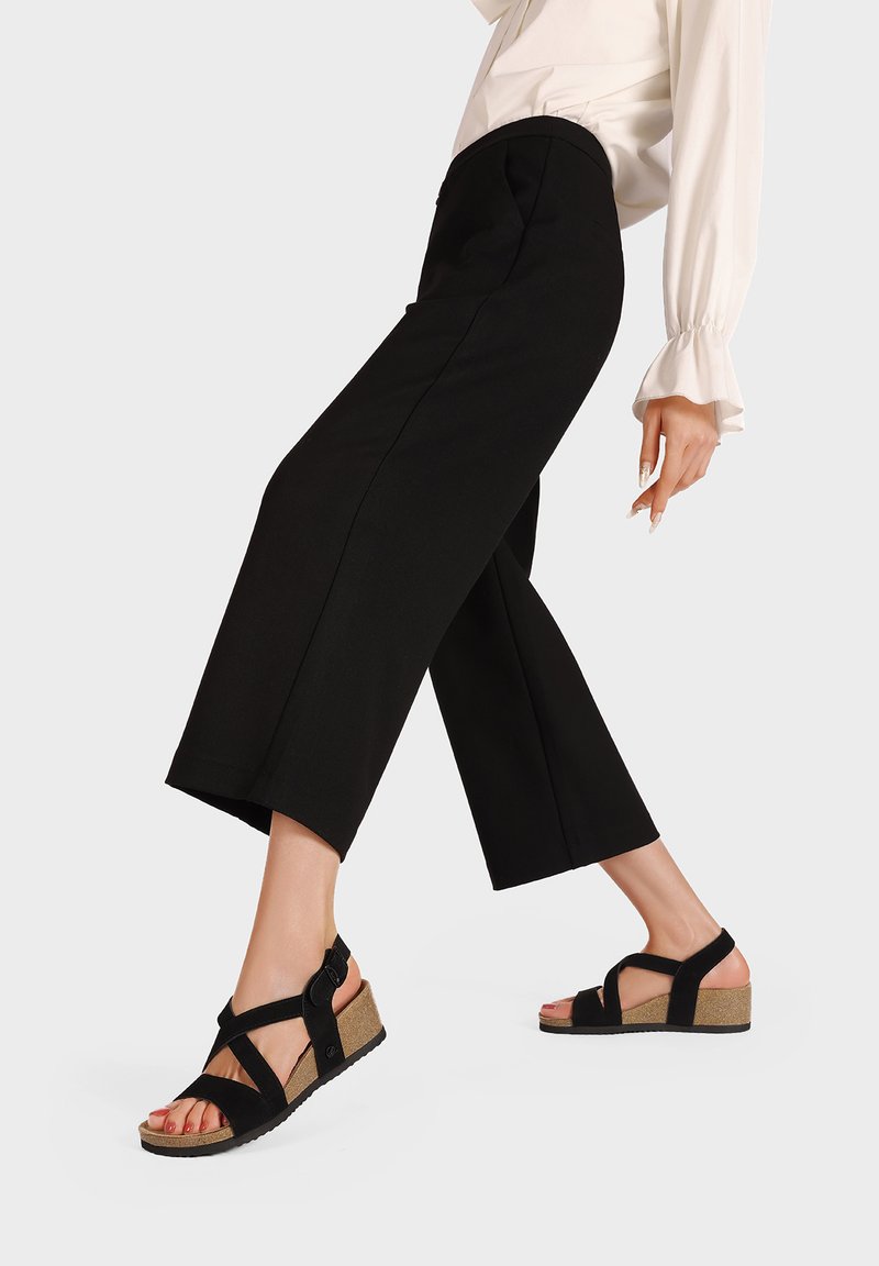 Sandali a zeppa neri con suola in sughero, dotati di fasce incrociate e cinturino alla caviglia regolabile. Texture del tessuto liscia con un design minimal.