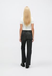 Juodos spalvos džinsai iš juodo džinso audinio su platėjančiomis kojų apačiomis ir aukštu liemeniu, matomi iš nugaros, turi dvi kišenes gale ir etiketę ant liemens juostos.