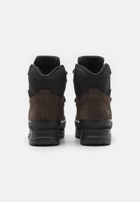 Brune tursko med en sort tekstiloverdel, suede detaljer og en teksturert gummisåle. Har en polstret krage og forsterkede snøringer.