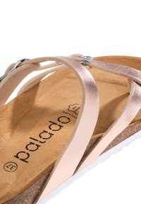 Ljusrosa metalliska sandaletter med en korkfotbädd, med tunna korsade remmar och en texturerad sula, som visar varumärket "palado."