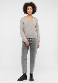 Jasnoszary, dziany sweter z dekoltem w kształcie litery V i luźnym krojem. Połączony z wysoko taliowanymi, wyblakłymi szarymi dżinsami i czarnymi sznurowanymi botkami.