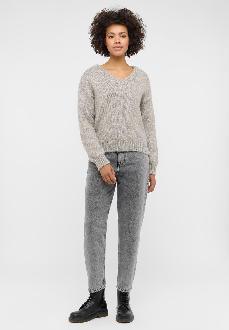 Jasnoszary, dziany sweter z dekoltem w kształcie litery V i luźnym krojem. Połączony z wysoko taliowanymi, wyblakłymi szarymi dżinsami i czarnymi sznurowanymi botkami.