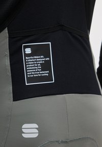 Lähikuva mustista ja harmaista pyöräilyn bibshortseista, joissa on etiketti, jossa lukee Sportful Riders Kit, ja kangaspaneeleissa logoja.