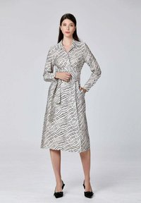 Robe à manches longues blanche avec des motifs de lignes abstraites noires, taille cintrée et col. Longueur mi-mollet avec une texture lisse.
