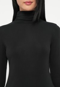 Zwarte langemouwen turtleneck top gemaakt van ribbelstof met een aansluitend ontwerp, voorzien van een hoge kraag en een soepele textuur.